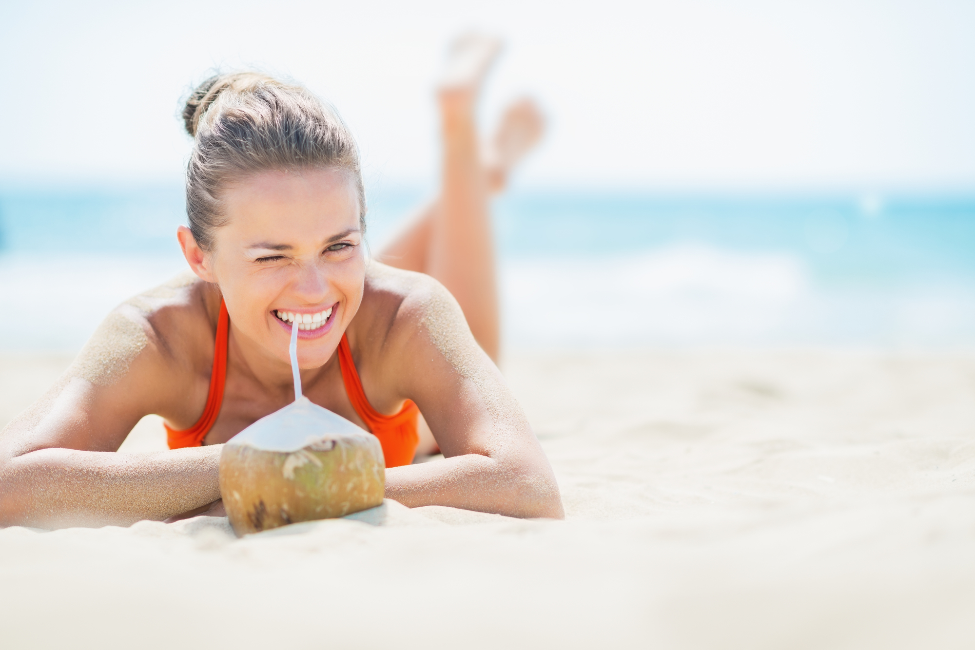 Young woman laying on beach and drinking coconut milk